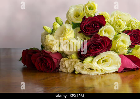 Un bouquet de fleurs roses rouges y compris en fleur jaune et des fleurs à la fois comme des bourgeons et en fleur. Assis sur une table en bois haut. Banque D'Images