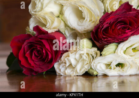 Un bouquet de fleurs roses rouges y compris en fleur et fleurs crème à la fois comme des bourgeons et en fleur. Assis sur une table en bois haut. Banque D'Images