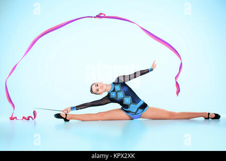 La jeune fille faisant la gymnastique danse avec ruban de couleur sur un fond bleu Banque D'Images