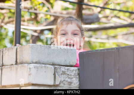 Cinq ans girl smiling regarda de derrière le mur Banque D'Images