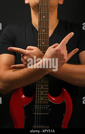 Homme avec guitare rouge montrant devil horns sur noir Banque D'Images