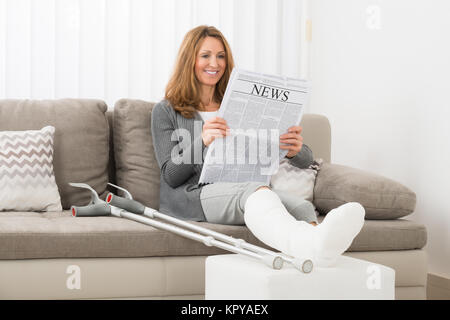 Femme avec fracture de la jambe Reading Newspaper Banque D'Images