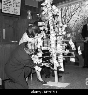 Années 1960, historiques, bien habillés dame dans un Kentucky Fried Chicken outlet se pencher avec une petite hache pour couper un arbre en bois 'Monnaie', une structure d'origine humaine qui a un certain nombre de dollars collé sur elle, USA. Banque D'Images