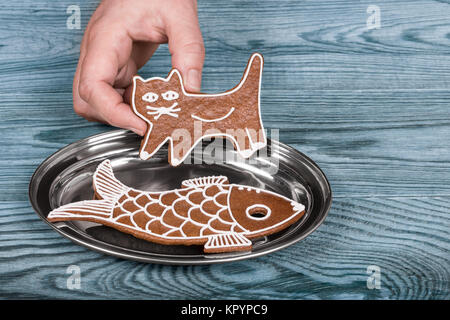 Chat et poisson. Noël mignon sur un plateau d'argent gingerbreads human hand holding the sweet kitty au-dessus de la plaque de bois brillant sur fond bleu. Banque D'Images