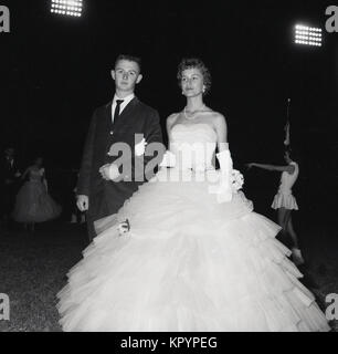 Années 1960, historique, du temps le soir, des projecteurs et défilé... un jeune homme en cravate noire accompagne une jeune femme portant une robe de bal magnifique collier et à l'extérieur à la fin de terme college ball ou un bal, USA. Banque D'Images