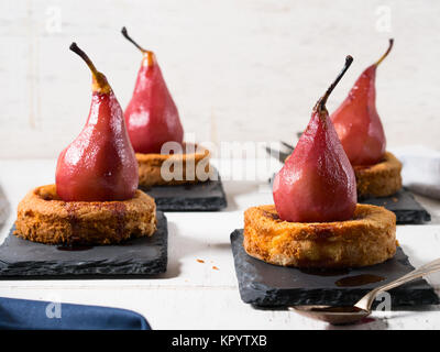 La polenta sucrée Mini tartelettes aux poires au vin rouge sur les plaques d'ardoise noire sur fond blanc en bois rustique Banque D'Images