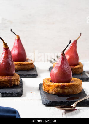 La polenta sucrée Mini tartelettes aux poires au vin rouge sur les plaques d'ardoise noire sur fond blanc en bois rustique Banque D'Images