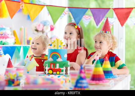 Kids Birthday party. Enfant blowing out candles on cake coloré. Maison décorée avec des bannières drapeau arc-en-ciel, de ballons, de confettis. Les transports et la ferme Banque D'Images