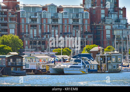 Un groupe de maisons flottantes thed jusqu'à un quai en face d'un grand complexe de condominiums au Victoria Harbour sur l'île de Vancouver (Colombie-Britannique) Canada. Banque D'Images