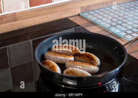 Cuire les saucisses dans une poêle sur une plaque à induction. Banque D'Images