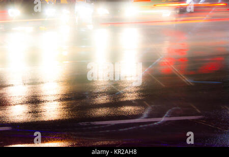 Le trafic de nuit floue des pluies sur les rues de la ville avec l'intersection des sentiers de lumière et des réflexions sur l'asphalte humide. Banque D'Images