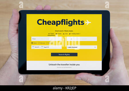 Un homme regarde le site Cheapflights sur son iPad tablet device, tourné contre une table en bois page contexte (usage éditorial uniquement) Banque D'Images