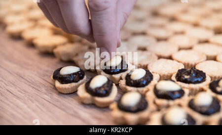 Décisions de sweet cupcakes avec garniture au chocolat et amandes. Détail de la main tout en décorant le Noël de coco sur un fond de pâte de bois. Banque D'Images