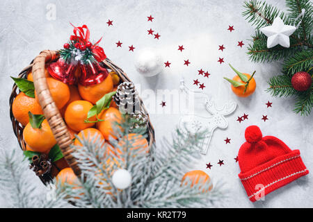 Composition de Noël avec des mandarines dans panier, red hat d'hiver, pommes de pin, sapin et jouets sur fond de béton lumineux. Vue d'en haut Banque D'Images
