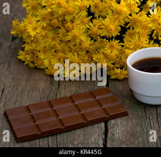 Bouquet de fleurs jaunes, un carreau de chocolat et de café, sur une table en bois, une nature morte Banque D'Images