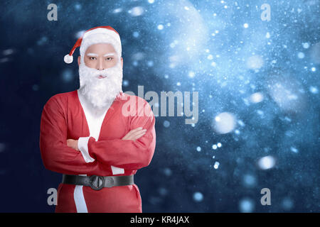 Bel asiatique homme en costume de Père Noël avec bras croisés contre l'arrière-plan de neige permanent Banque D'Images