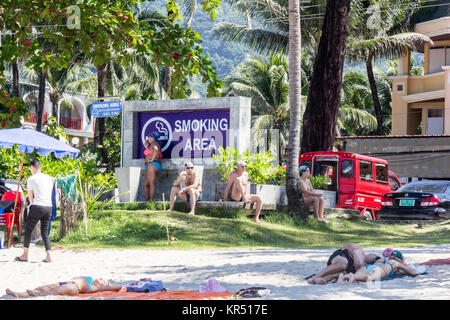 Les touristes de fumer des cigarettes dans une zone fumeurs, Patong Beach, Phuket, Thailand Banque D'Images
