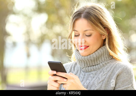Portrait d'une femme des messages sur un téléphone intelligent à l'extérieur en hiver Banque D'Images