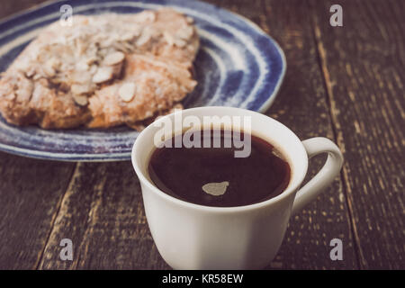 Tasse de café avec un croissant aux amandes avec trouble sur la plaque en céramique bleue Banque D'Images