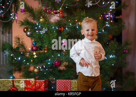 Cute Blonde hair petit garçon près de la cheminée et des cadeaux sous l'arbre de Noël. Banque D'Images