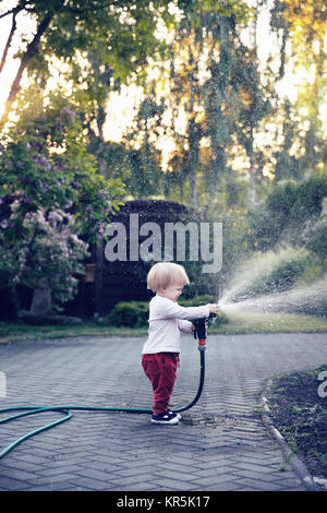 Baby girl d'arroser le jardin avec le tuyau Banque D'Images