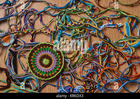 Différents types de bracelets colorés tricotés et boucles d'sont chaotiquement allongé sur la table. Dans le coin inférieur gauche, il y a un grand verre d'authenticité en tricot Banque D'Images