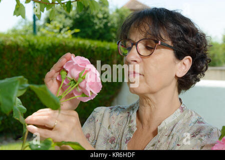 Femme mature qui sent la rose de son jardin Banque D'Images