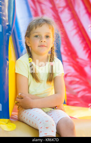 Fille de cinq ans naprygalis sur un grand trampoline gonflable s'assit pour se reposer Banque D'Images