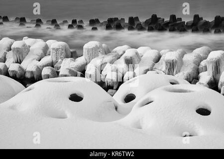 Les disjoncteurs d'onde couverte de neige sur une plage rocheuse en hiver. Banque D'Images