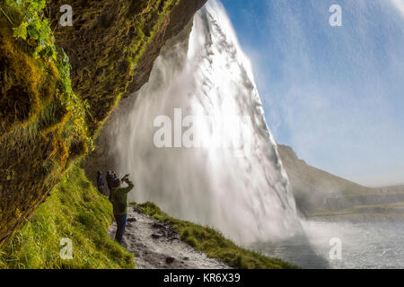 Personnes debout sur un chemin étroit sous une cascade cascade sur une falaise. Banque D'Images