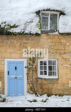 Chalet de chaume recouvert de neige avec une porte d'entrée bleu clair à Broadway en décembre. Broadway, Cotswolds, Worcestershire, Angleterre Banque D'Images