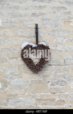 Couronne de Noël en forme de coeur déco a de pommes de pin avec de la neige sur un mur de chalets à Noël. Chedworh, Cotswolds, Gloucestershire, Angleterre, Banque D'Images