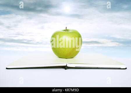 Livre ouvert avec une pomme verte au-dessus de elle avec sky sur l'arrière-plan Banque D'Images