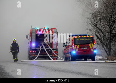 SALO, FINLANDE - le 16 février 2014 : Firefighter émerge de la fumée intense sur les lieux d'un incendie de Salo, usine de ciment avec deux camions d'incendie sur la rue. Banque D'Images