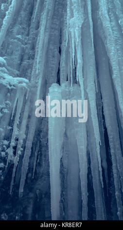 Mur de glace raide glissant vertical avec de longs glaçons dans une grotte. Cascade de glace d'eau. Banque D'Images