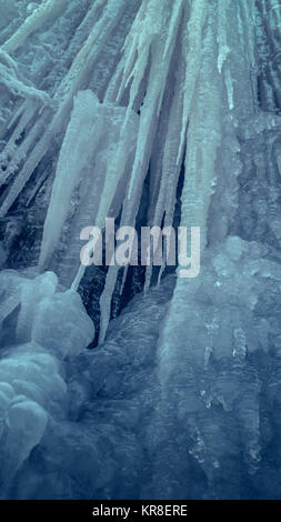 Mur de glace raide glissant vertical avec de longs glaçons dans une grotte. Cascade de glace d'eau. Banque D'Images