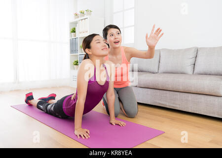 Smiling jolie fille faisant du yoga dans la salle de séjour et d'étirements méditation rêverie corps quand son professeur de fitness à domicile personnel d'entraînement de l'enseignement de la classe. Banque D'Images