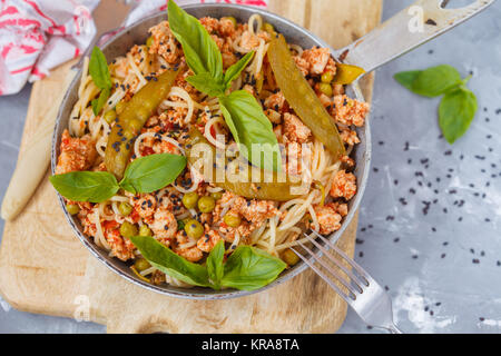 Des pâtes spaghetti à la farcissure prг©parent de poulet, des pois verts et basilic dans une poêle, sur fond rustique. Banque D'Images