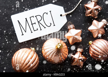 Étiquette avec texte français Merci veut dire merci. Boules de bronze sur fond de papier noir avec des flocons de neige. Décoration de Noël ou la texture. Voir mise à plat Banque D'Images