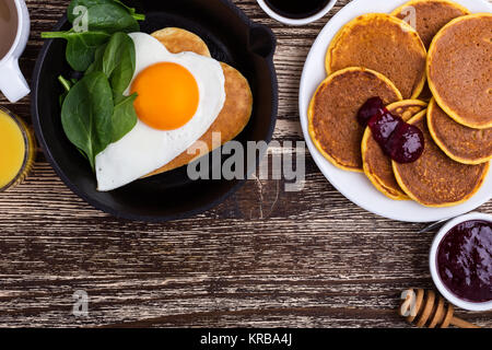 Valentine's day breakfast ou un brunch. Forme de coeur fait maison et d'œufs au plat en fonte poêle à crêpes aux épinards, des crêpes avec de la confiture de citrouille, orange Banque D'Images