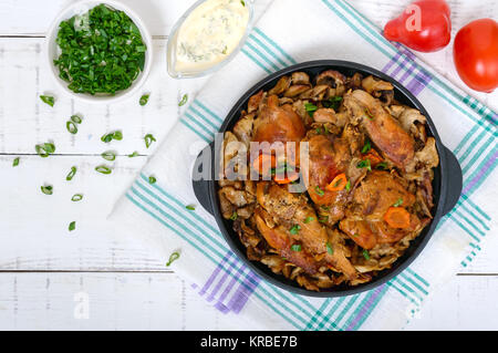 Morceaux de lapin frit avec champignons des bois sur un poêle en fonte sur un fond de bois blanc.