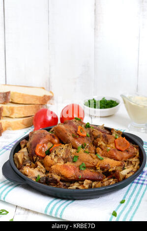 Morceaux de lapin frit avec champignons des bois sur un poêle en fonte sur un fond de bois blanc.
