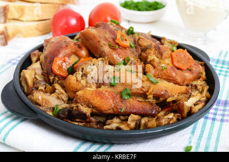 Morceaux de lapin frit avec champignons des bois sur un poêle en fonte sur un fond de bois blanc.