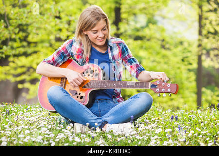 Young woman sitting in park et accordage guitare acoustique Banque D'Images