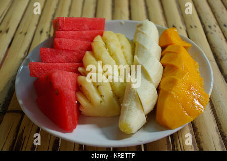 Plaque blanche avec tranches de fruits : melon, mangue, banane, ananas. sur la table dans un café. Banque D'Images