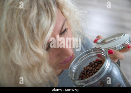 Fille blonde avec les cheveux bouclés est odeur de grains de café dans le pot en verre Banque D'Images