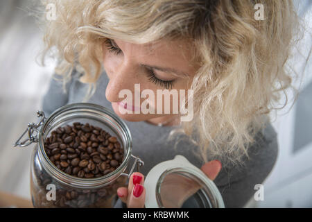 Fille blonde avec les cheveux bouclés est odeur de grains de café dans le pot en verre Banque D'Images