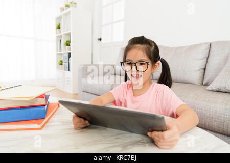 Happy pretty little girl a fini l'école à domicile et à l'aide de tampon mobile recherche calculateur en ligne drôle jeu vidéo relaxant. Banque D'Images