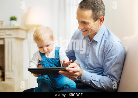 Calme genre père montrant une tablette moderne à son petit enfant Banque D'Images