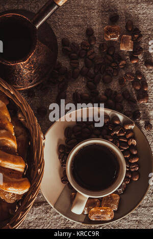 Tasse de café sur le textile avec les légumineuses, le sucre candi, pots, panier et gâteau Banque D'Images